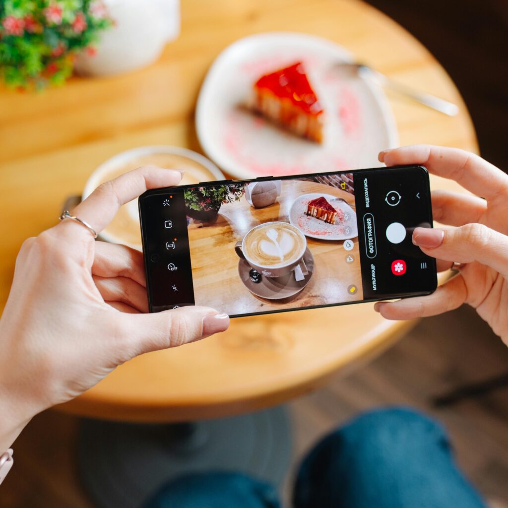 A woman captures a latte and cake slice with her smartphone in a café setting.