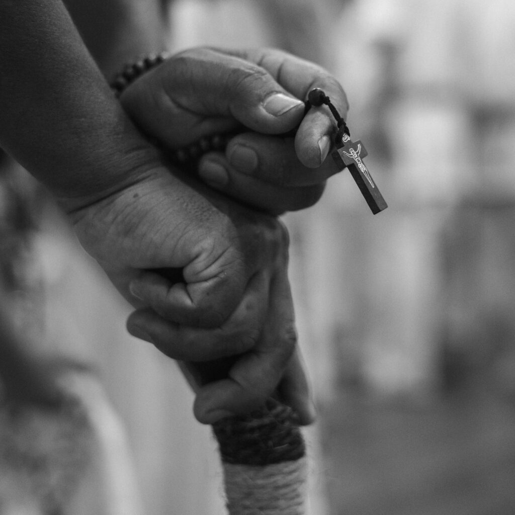 Black and white photo of hands holding a rosary with cross, symbolizing faith and spirituality.